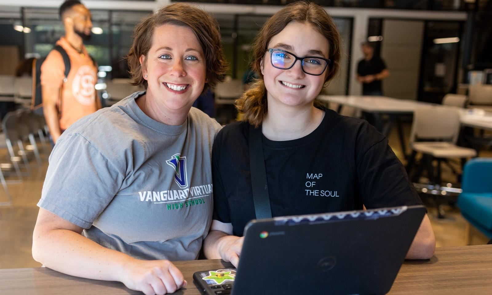 An adult and student smile while using a laptop
